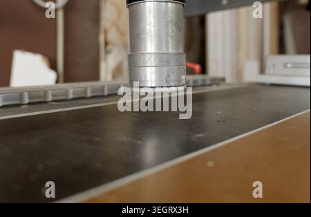 Cnc router machine head positioned above a dusty surface, featuring an aluminum body and a fuzzy white tip, preparing for precision cutting or engravi Stock Photo