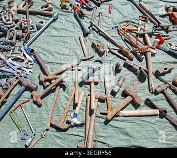 Various rusty hand tools are scattered on a wrinkled green tarp at an outdoor flea market. Old hammers, wrenches, screwdrivers, and pliers are visible Stock Photo
