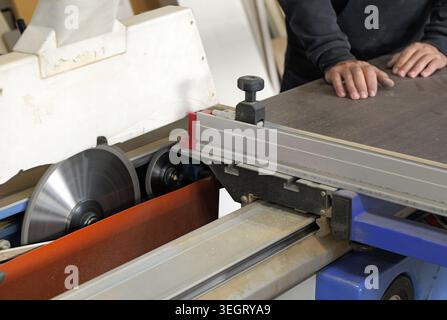 Woodworker operating an industrial panel saw, using the powerful machine for precision cutting of wooden panels in a production workshop, focusing on Stock Photo