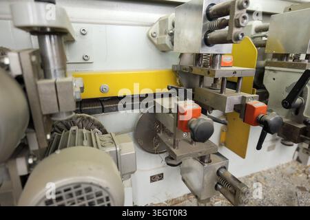 Close up of an industrial edge banding machine, showing mechanical parts, motors, and a conveyor belt, representing automated manufacturing and woodwo Stock Photo