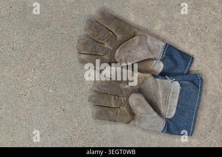 Pair of dirty protective leather work gloves on concrete floor flat lay. Stock Photo