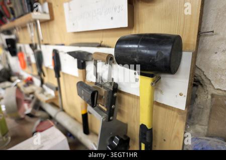 Various metal and rubber hand tools hanging on a wooden wall storage system, creating an organized yet functional workspace for craft, hobby, and home Stock Photo