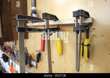 Collection of woodworking clamps hanging neatly on a wooden wall, representing organized tools and equipment in a busy carpentry workshop environment Stock Photo