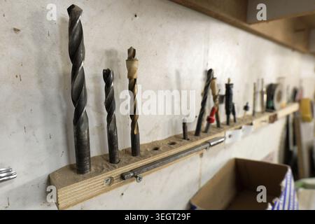 Assortment of used metal drill bits and tools standing in a custom made wooden organizer, covered in wood dust, demonstrating a practical workshop set Stock Photo