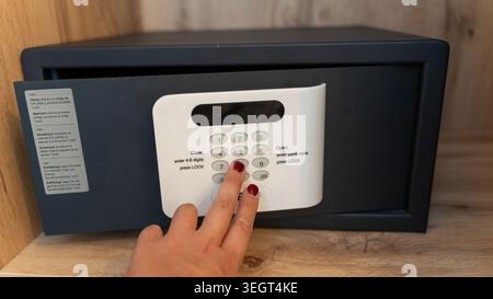 Close up of woman entering code on electronic hotel safe with digital keypad for secure storage of valuables. Stock Photo