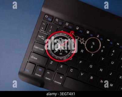 A red compass keychain is placed directly on top of the character keys of a black computer keyboard. Stock Photo