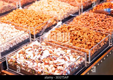 Variety of premium roasted nuts, walnuts, pistachios, and mixed dried fruits with coconut chips displayed in clear boxes at La Boqueria public market Stock Photo