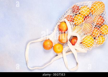 Reusable string bag filled with oranges and blood oranges on a light blue background, flat lay promoting plastic free shopping, sustainable living and Stock Photo
