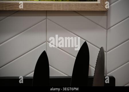 Close Up of Knife Tips Hanging on Magnetic Strip in Kitchen with White Tiled Background Stock Photo