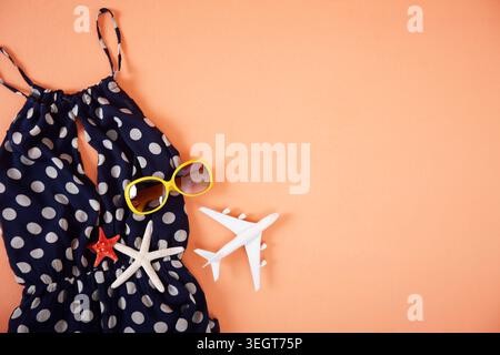 A blue polka-dot swimsuit, sunglasses, starfish, and a toy airplane are arranged on a peach-colored background. Stock Photo