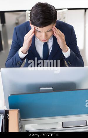 A businessman rubs his temples in frustration while staring at his computer screen. Stock Photo