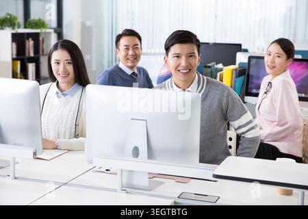A group of young professionals smile while working on computers in a modern office. Stock Photo