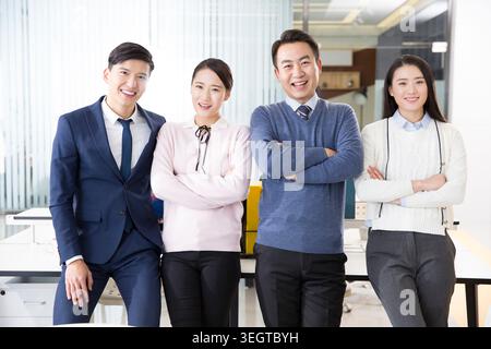 A group of colleagues in a modern office, smiling and standing together with their arms crossed. Stock Photo