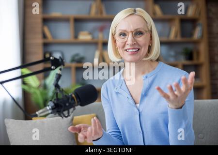 Happy woman creating audio content for blog, broadcasting online radio show from domestic studio, speaking into professional microphone, communicating digitally Stock Photo
