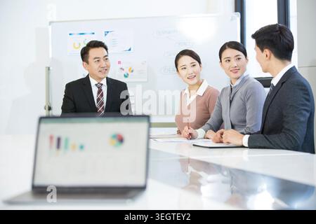 A group of businesspeople sitting around a white table, smiling at a laptop screen displaying a colorful graph. Stock Photo