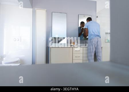 Male standing at bathroom vanity, wiping face with towel, in light blue tee, copy space Stock Photo