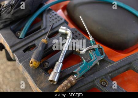 Mechanic tools including screwdriver wrench air blow gun lying on orange machine part preparing for maintenance and repair work outdoors showing pract Stock Photo