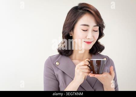 A young woman in a business suit holds a coffee cup, smiling as she sips her morning coffee. Stock Photo