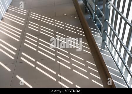 Sunlight shining through metal fence creating striped shadow pattern on tiled walkway creating calm and peaceful outdoor atmosphere with strong contra Stock Photo