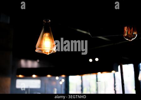 Vintage glass pendant light bulb glowing warm yellow illuminating dark interior room creating cozy atmospheric mood with blurred background Stock Photo