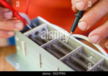Focused electrician performing precise repair using multimeter tool to test electrical coil equipment with steady hand during routine maintenance chec Stock Photo