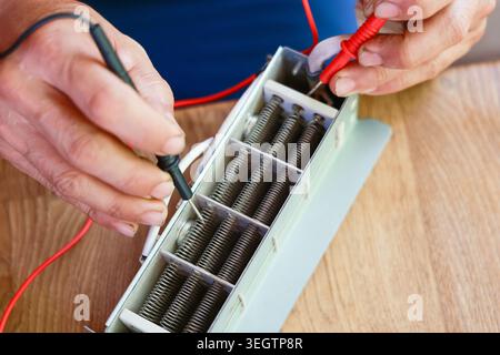 Focused technician hand testing electronic component using multimeter probe during careful repair work measuring voltage on wooden table displaying in Stock Photo