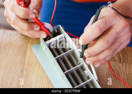 Focused technician hand test battery pack using multimeter device for electronic repair on wooden table checking voltage current power supply maintena Stock Photo