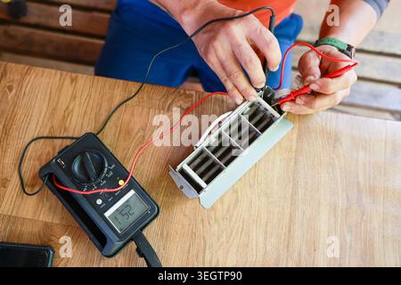 Focused electrician hands test industrial electrical component using digital multimeter on wood table during daily repair work taking careful measurem Stock Photo