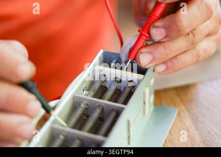 Focused electrician hand carefully testing electrical component using red and black multimeter probe during attentive repair process on wooden workspa Stock Photo