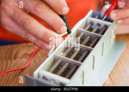 Focused electrician testing complex electrical equipment using multimeter and probe measuring precise voltage current on circuit with careful hands pe Stock Photo