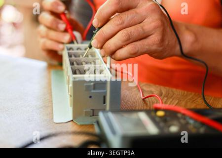 Electrician hands demonstrate intense focus testing electronic component using multimeter during precise repair and maintenance work on industrial equ Stock Photo