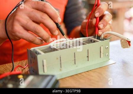 Focused electrician testing electrical component with multimeter probe in hand during careful repair work on wire circuit measuring voltage to ensure Stock Photo