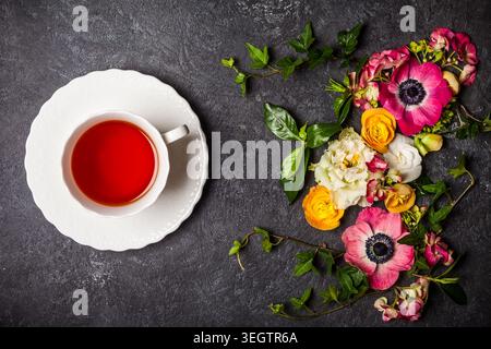 Cup of tea and various flowers on black background. Overhead view with copy space Stock Photo