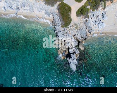 Aerial view of a pebble beach and rocky coastline with turquoise clear water and green vegetation in Pallini, Greece. Stock Photo