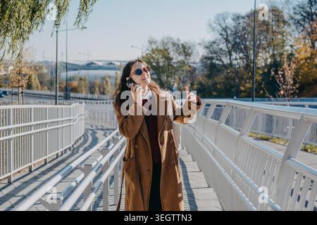 Woman walks on pedestrian bridge while talking on mobile phone. Corporate phone call on the go, female professional business commuting, real time Stock Photo