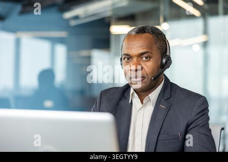 Experienced male call center employee wearing a headset while providing online customer service or participating in a virtual meeting with a laptop, i Stock Photo