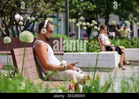 Man using smartphone sitting on city street at summer Stock Photo