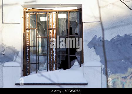 A stark winter scene featuring a broken window pane on a weathered wall heavily dusted with fresh snow below Stock Photo