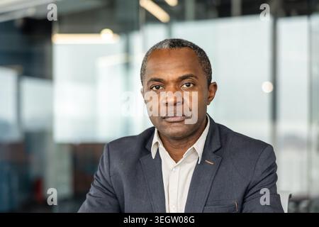 Mature businessman in a suit jacket looks confidently at the camera in a modern office headshot, conveying professionalism, leadership, experience and Stock Photo
