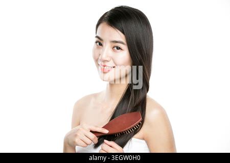 Portrait of young smiling woman brushing her long straight hair Stock Photo
