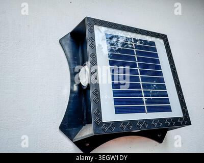 Modern solar powered LED outdoor wall light with motion sensor mounted on a white exterior wall, renewable energy and smart home concept Stock Photo