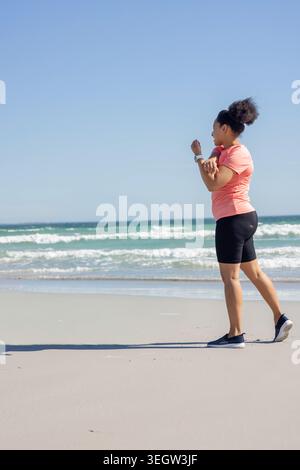 African American woman standing on shore checking smartwatch coral-top black-shorts, copy space Stock Photo