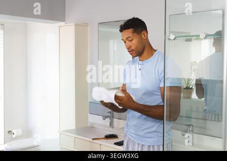 Mid-adult African American man holding white towel in light blue henley at vanity with mirror Stock Photo