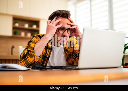 Freelancer working on laptop remotely from home, he is frustrated and angry. Stock Photo