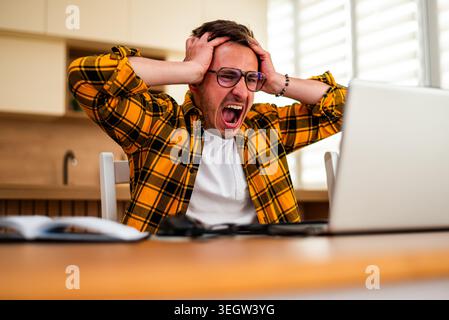 Freelancer working on laptop remotely from home, he is having nervous breakdown. Stock Photo