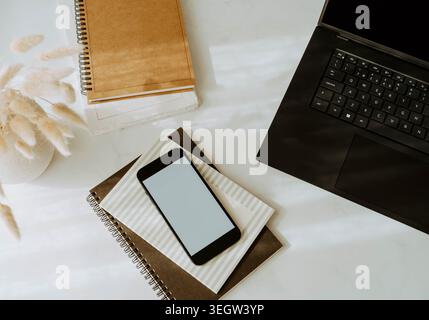 Workspace flat lay with laptop, smartphone and notebooks on a white desk, minimalist home office scene with soft light and productivity mood Stock Photo