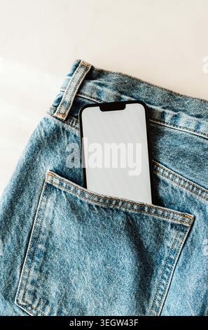 Smartphone with blank screen in a blue denim jeans pocket, casual fashion and technology concept with copy space for app or mobile design. top view Stock Photo