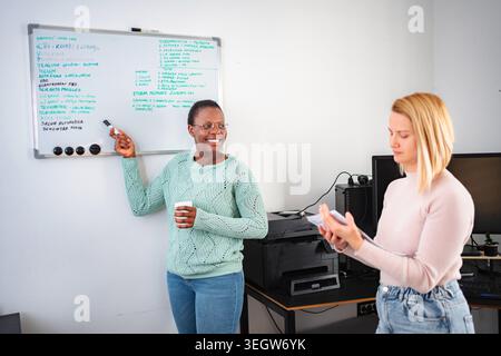 Businesswomen collaborating on project, smiling and discussing in office Stock Photo