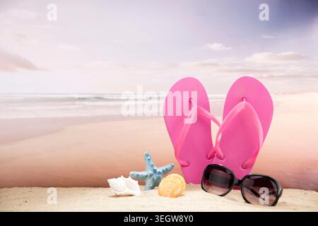 A pair of pink flip-flops and sunglasses sit on a sandy beach, surrounded by seashells and a starfish. Stock Photo