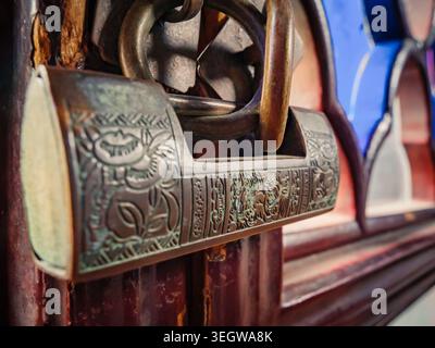 Old padlock hangs on wooden door at a market in the afternoon light showing intricate design and rusty texture Stock Photo